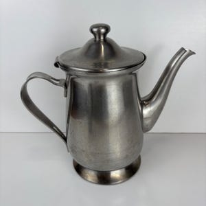 May include: A stainless steel teapot with a curved spout, a handle, and a lid with a small knob. The teapot has a rounded base and a brushed metal finish. The design is simple and functional.