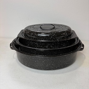 May include: A set of three nested black roasting pans with white speckled enamel finish. Each oval-shaped pan features side handles and a matching lid with a central handle. The pans are stacked vertically, showing a consistent design.