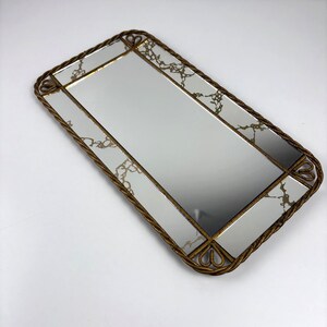 May include: Rectangular mirror with a gold-toned, rope-style frame. The mirror surface is divided into sections with gold trim and decorative accents. The frame has heart-shaped details at the corners, adding elegance.
