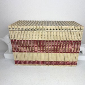 May include: A set of twenty-four vintage books titled "World War II Illustrated." The spines are a deep red with gold lettering, and the covers are a cream colour. The books are arranged in a neat row, with the numbers 1 to 24 visible.