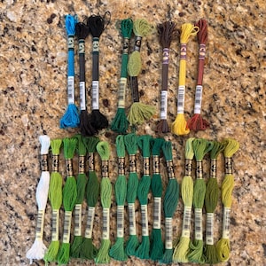 May include: A collection of embroidery floss in various colors, including blue, black, green, brown, yellow, and red. The floss is arranged in neat bundles, showcasing a range of shades and hues. Ideal for embroidery, cross-stitch, and other needlecraft projects.