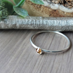 May include: A silver ring with a small, round, amber-coloured gemstone.