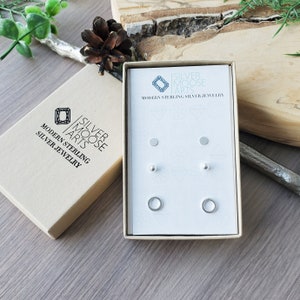 May include: A set of three sterling silver earrings in a white box. The earrings are a small circle, a small dot, and a small ball. The box has the text "Silver Moose Arts" and "Modern Sterling Silver Jewellery" printed on it.