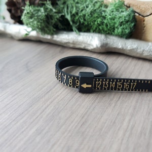 May include: Black ring sizer with gold numbers from 6 to 17. The sizer is made of flexible plastic and has an arrow to indicate the size.