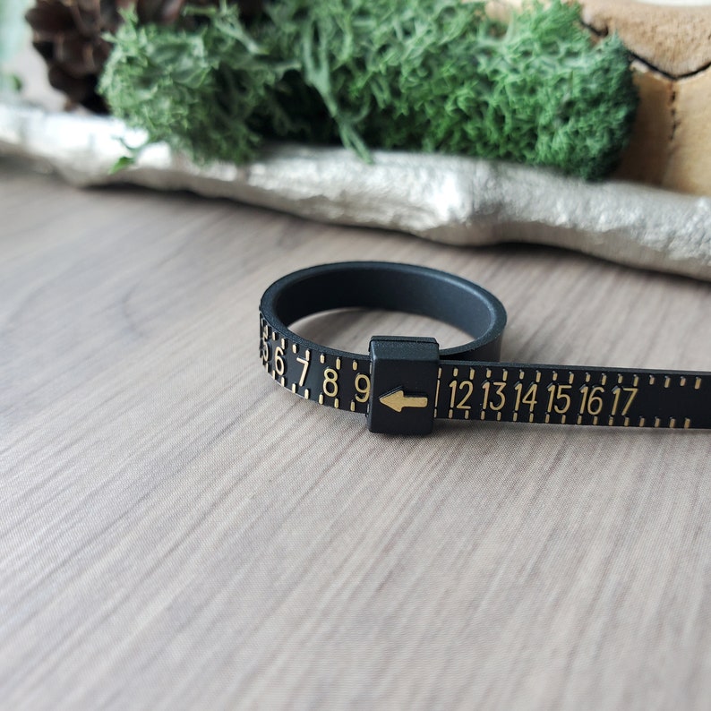 May include: Black ring sizer with gold numbers from 6 to 17. The sizer is made of flexible plastic and has an arrow to indicate the size.