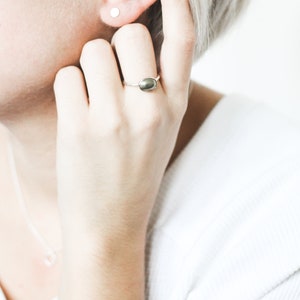 May include: A close-up of a person's hand wearing a silver ring with a dark green oval-shaped stone. The person is also wearing a small silver stud earring in their left ear.