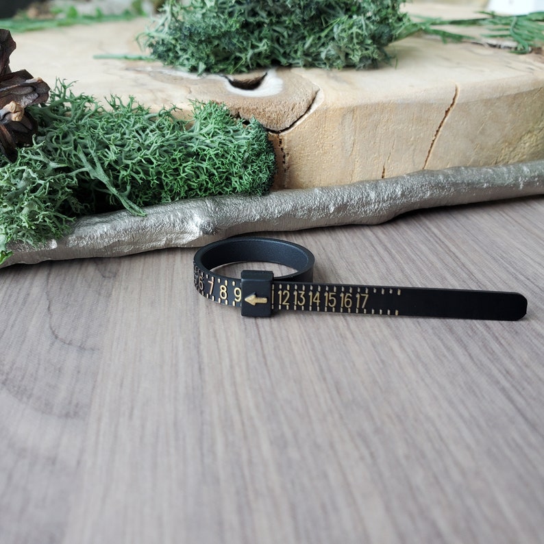 May include: Black ring sizer with gold numbers and an arrow. The sizer is marked with sizes 7 through 17.