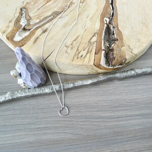 May include: A silver chain necklace with a simple open heart pendant. The necklace is laying on a wooden surface.