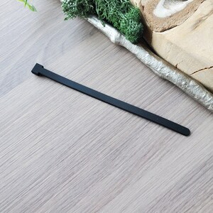 May include: A black rubber cable tie, also known as a zip tie, is shown on a light brown wooden surface.