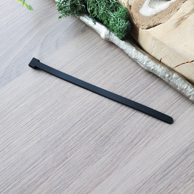 May include: A black rubber cable tie, also known as a zip tie, is shown on a light brown wooden surface.