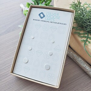 May include: A box of sterling silver earrings in a variety of shapes and sizes. The box is white with a light blue background and the text "SILVER MOOSE ARTS MODERN STERLING SILVER JEWELRY" printed on the front.