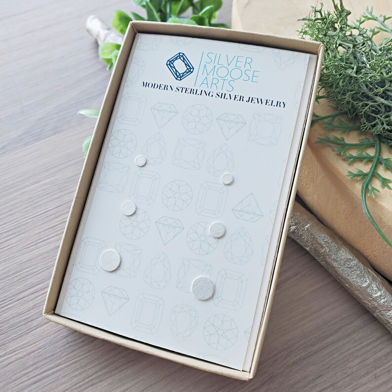 May include: A box of sterling silver earrings in a variety of shapes and sizes. The box is white with a light blue background and the text "SILVER MOOSE ARTS MODERN STERLING SILVER JEWELRY" printed on the front.