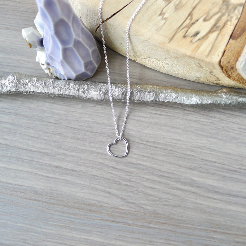 May include: A silver chain necklace with a delicate open heart pendant.