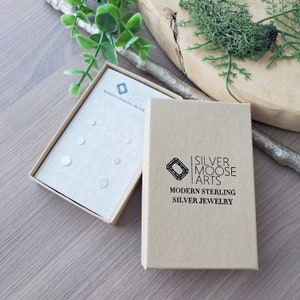 May include: A set of small, round, sterling silver earrings in a white box with the text "Silver Moose Arts Modern Sterling Silver Jewelry".