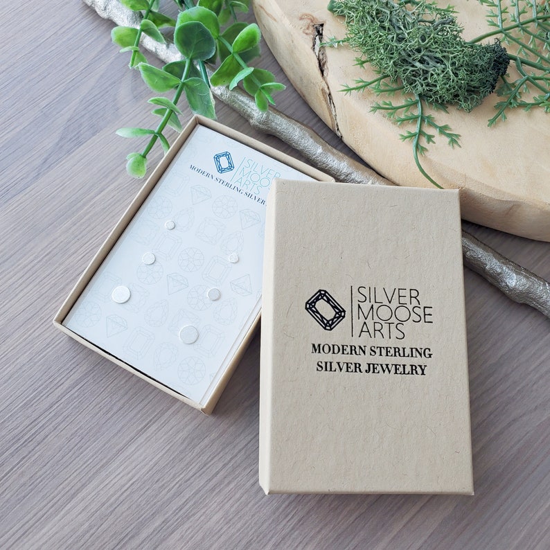 May include: A set of small, round, sterling silver earrings in a white box with the text "Silver Moose Arts Modern Sterling Silver Jewelry".