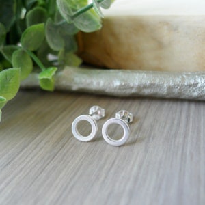 Peut inclure: Une paire de boucles d'oreilles à tige en argent présentant un design simple en forme d'anneau ouvert circulaire. Chaque boucle d'oreille a une finition métallique polie et comprend une fermeture à tige standard, offrant une esthétique géométrique.