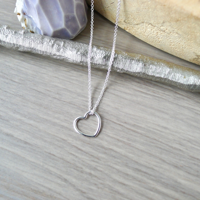 May include: A silver chain necklace with a delicate open heart pendant.