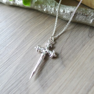 May include: A silver pendant necklace with a detailed, ornate cross design. The cross is shaped like a sword with intricate details.