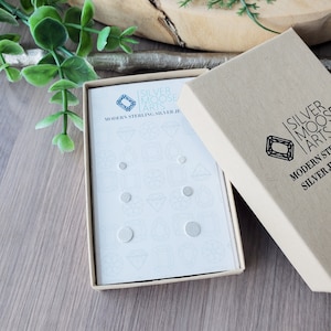 May include: A white box with a blue logo that says "Silver Moose Arts" and the text "Modern Sterling Silver Jewelry". The box contains a set of silver stud earrings.
