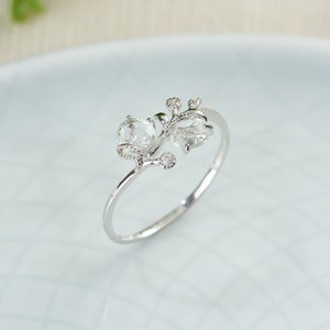 May include: A silver ring with two clear gemstones set in a delicate branch design.