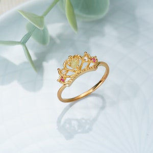 May include: A gold crown ring with a light green stone and pink accents.