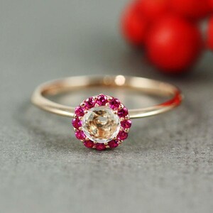 May include: A rose gold ring with a clear gemstone surrounded by a halo of pink rubies.