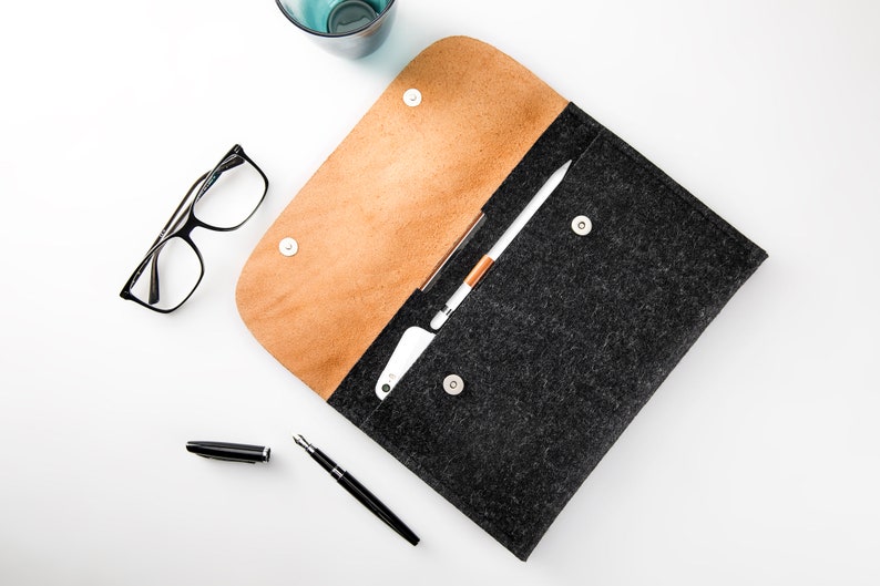 May include: A black felt and brown leather envelope with a white stylus and a black pen on a white surface.