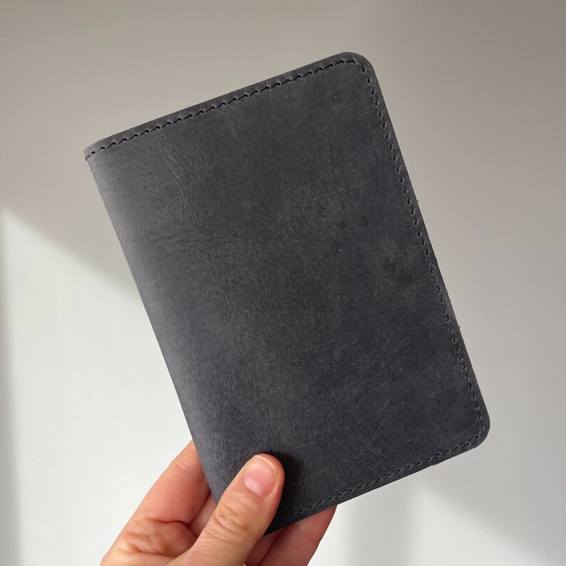 May include: A dark gray leather passport holder with stitched edges.