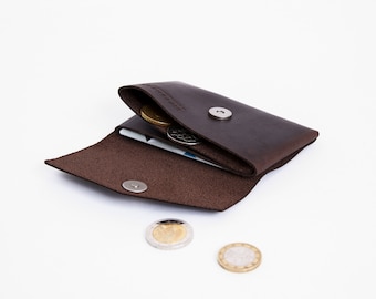 May include: A brown leather wallet with a snap closure and a coin pocket. The wallet is open and there are coins inside.