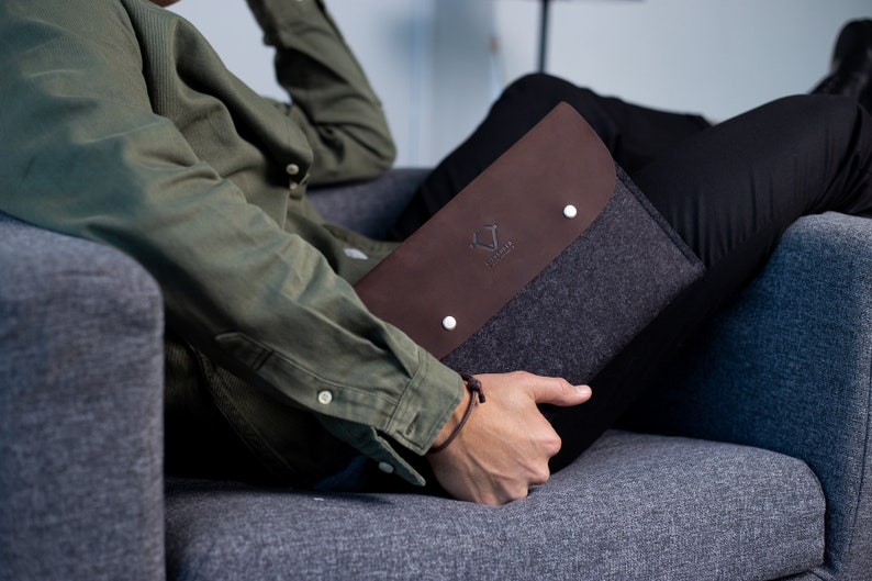 May include: A brown leather and gray felt laptop sleeve with a white logo that says "The Felt Co."