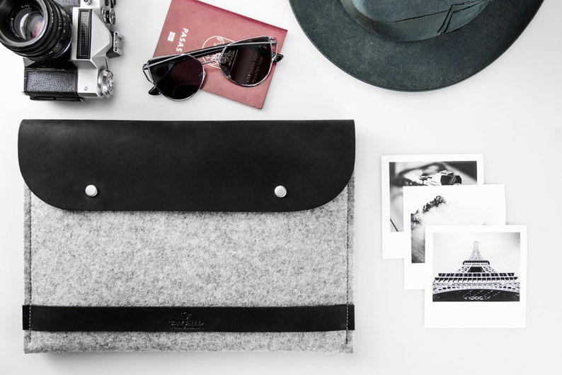 Leather and felt laptop case on the table. Near it there are sun glasses, photos, passport, hat and vintage camera.