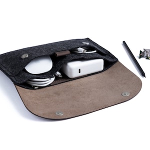 May include: A black felt pouch with a brown leather flap, open to reveal a white power adapter, white charging cables, and a white wireless mouse. The pouch has a snap closure and is lined with brown felt.