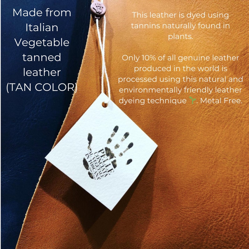 May include: Close-up of a tan leather swatch with a white tag attached. The tag has a black handprint with the text "PELLE CONCIATA AL VEGETALE IN TOSCANA". The text on the leather swatch reads "Made from Italian Vegetable tanned leather (TAN COLOR)" and "This leather is dyed using tannins naturally found in plants. Only 10% of all genuine leather produced in the world is processed using this natural and environmentally friendly leather dyeing technique. Metal Free."