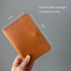May include: A brown leather wallet with stitched edges. It measures 6.7 inches by 4.3 inches. Minimalist design. Compact size.