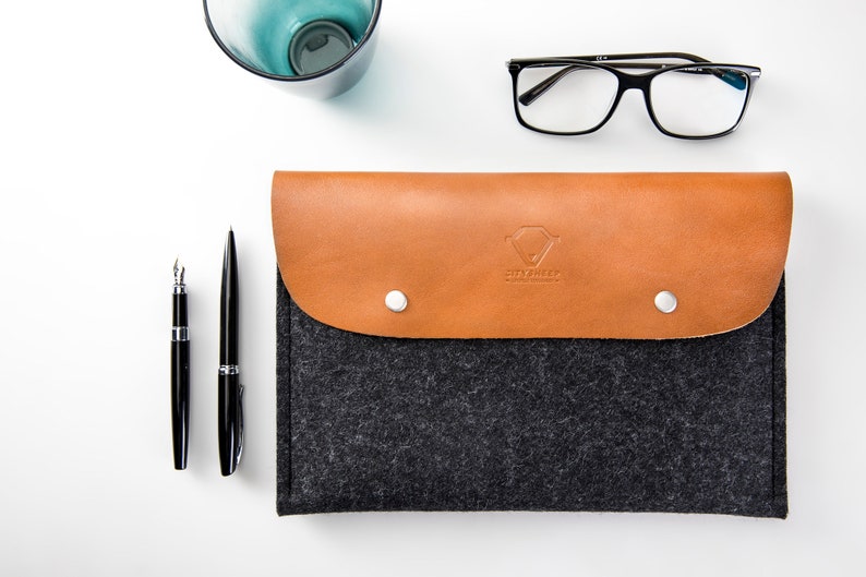 May include: A gray felt laptop sleeve with a brown leather flap and a snap closure. The flap has a logo that says "CitySheep" in a diamond shape.