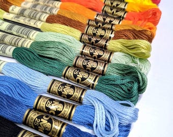 May include: A collection of 25 DMC embroidery floss spools in various colors, including purple, pink, orange, yellow, green, blue, and black. Each spool has a gold label with the DMC logo and the number 25.