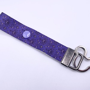 May include: Purple patterned wristlet keychain with a silver-tone clasp and a light purple button closure. The keychain features a decorative pattern and a Mickey Mouse-shaped clasp.