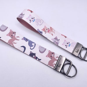 May include: Two white keychains with a repeating pattern of cartoon cats. The keychains have silver key rings.