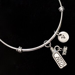 May include: A silver expandable bracelet with a charm of a gin bottle and the word "tonic" and a charm with the number "2".