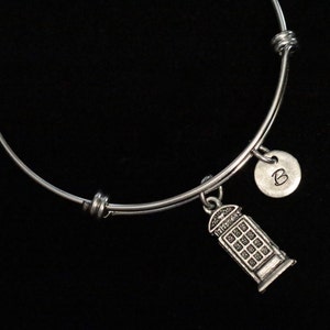 May include: A silver bangle bracelet with a charm of a London telephone booth and a silver charm with the letter "B" engraved on it.