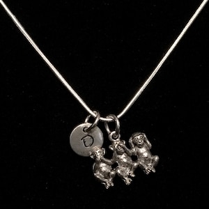 May include: Silver necklace with three small monkey charms and a silver charm with the letter 'D' on it.