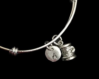 Op de afbeelding: Een zilveren armband met een spoel garen bedel en een gepersonaliseerde bedel met de letter "A".
