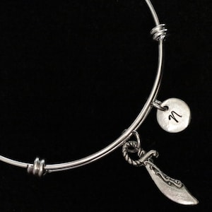 Op de afbeelding: Een zilveren uitbreidbare armband met een zilveren bedel in de vorm van een zwaard en een zilveren bedel met de letter "M" erop gegraveerd.