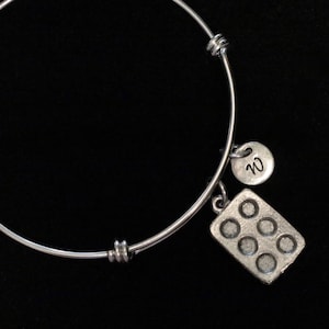 Può includere: Un braccialetto espandibile in argento con due ciondoli. Un ciondolo è un disco rotondo con la lettera "W" incisa. L'altro ciondolo è una teglia per muffin in miniatura.
