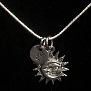 May include: A silver necklace with a sun and moon charm and a small charm with the letter 'E' engraved on it.