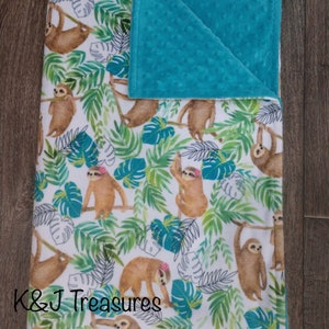 May include: A white and green baby blanket with a pattern of sloths hanging from trees. The blanket has a turquoise minky backing.