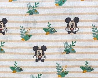 Puede incluir: Una tela blanca con rayas marrones y un patrón repetido de Mickey Mouse y ramas verdes con hojas.