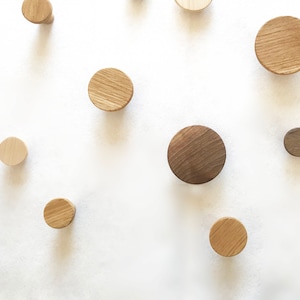 Könnte beinhalten: Ein Satz aus Holz-Wandhaken in verschiedenen Größen und Brauntönen und Beige. Die Haken sind rund und haben eine glatte Oberfläche.