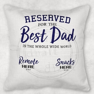 May include: White throw pillow with blue text that reads "RESERVED FOR THE Best Dad IN THE WHOLE WIDE WORLD". The pillow also has two circles with the text "Remote HERE" and "Snacks HERE" in black.