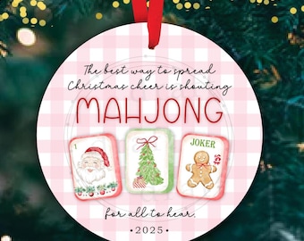 May include: Round Christmas ornament with a red ribbon. The ornament has a pink and white checkered background with the word "MAHJONG" in red. It features three illustrated cards and the text "The best way to spread Christmas cheer is shouting Mahjong for all to hear. 2025."